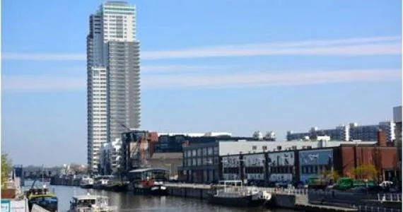 Vue urbaine en bord de canal avec immeuble moderne en verre bleu-vert, bâtiments anciens en brique et ciel dégagé.