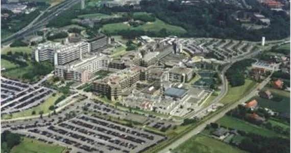 Vue aérienne de site industriel avec bâtiments polygonaux modernes, routes d'accès, zones vertes et chantiers adjacents.